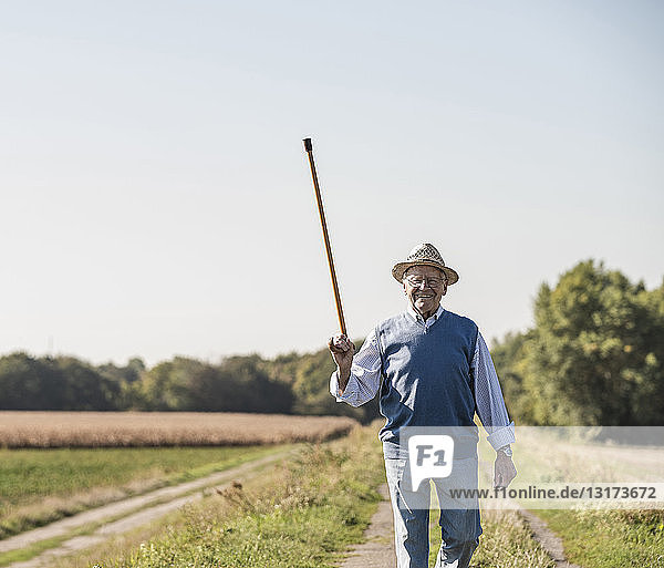 Älterer Mann geht auf den Feldern  grüßt mit seinem Gehstock