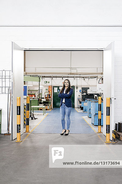 Selbstbewusste Frau  die in einem High-Tech-Unternehmen arbeitet  steht mit verschränkten Armen in einer Fabrikhalle