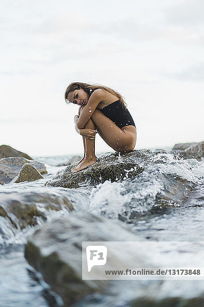 Hübsche junge Frau im Badeanzug auf einem Felsen im Meer sitzend