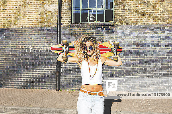 Porträt einer lächelnden jungen Frau mit Skateboard in der Stadt