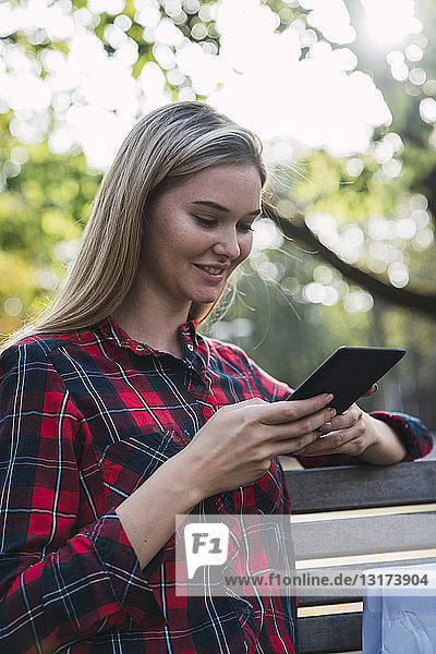 Smiling young woman sitting on bench outdoors using mini tablet