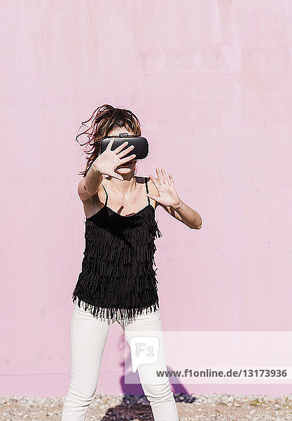 Junge Frau mit VR-Brille vor rosa Wand