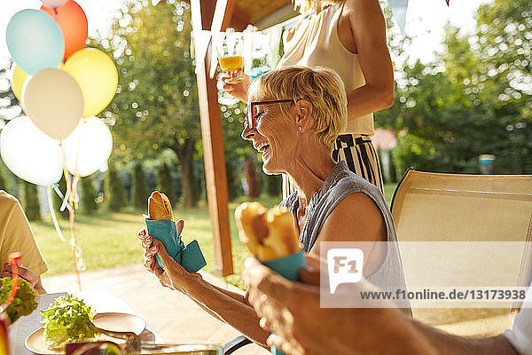 Glückliche Frau isst einen Hot Dog auf einer Gartenparty