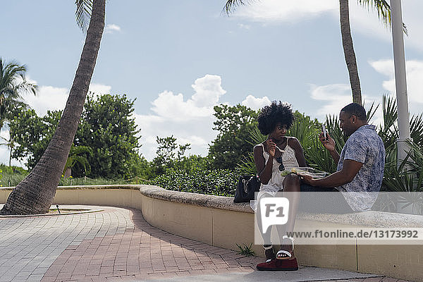 USA  Florida  Miami Beach  junger Mann beim Fotografieren einer Freundin  die in einem Park einen Salat isst