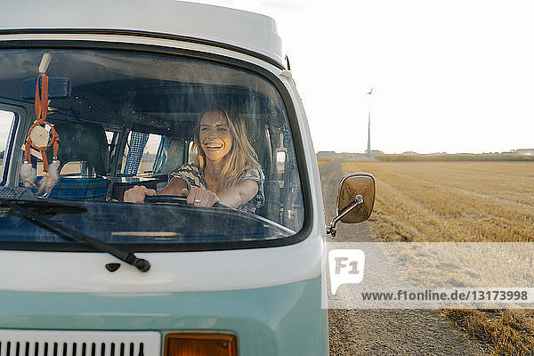 Happy young woman driving camper van in rural landscape