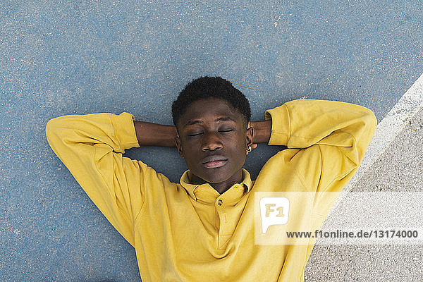 Junger schwarzer Mann schläft auf dem Boden  die Hände hinter dem Kopf