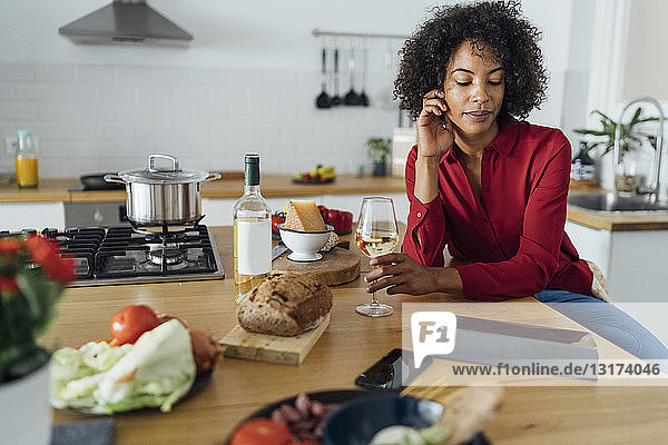Frau sitzt in der Küche mit einem Glas Weißwein und benutzt ein digitales Tablett