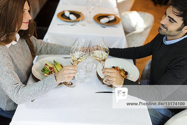 Lächelndes Paar beim Anstossen von Weingläsern in einem Restaurant