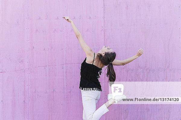 Glückliche junge Frau bewegt sich vor rosa Wand