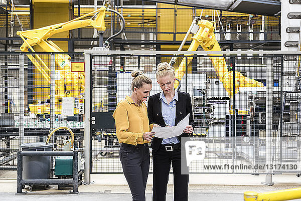 Two women discussing plan in factory shop floor with industrial robot