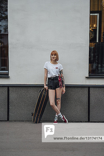 Porträt einer auf dem Bürgersteig stehenden jungen Frau mit Carver-Skateboard