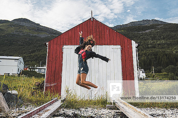 Junge Frau springt vor rote Scheune in Nordnorwegen