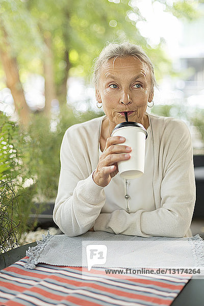 Ältere Frau mit einem Getränk in einem Außencafé