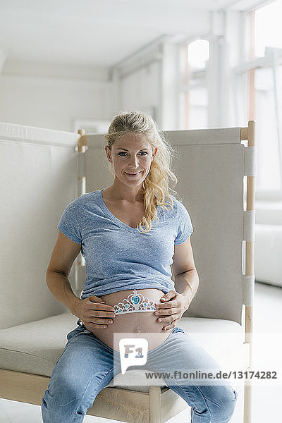 Porträt einer lächelnden schwangeren Frau  die das Diadem am Bauch hält