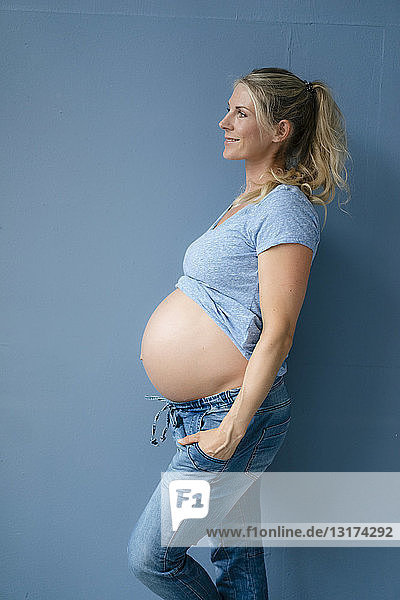 Lächelnde schwangere Frau steht an blauer Wand