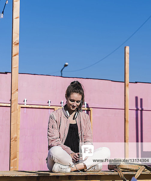 Junge Frau sitzt auf Bahnsteig und benutzt Mobiltelefon
