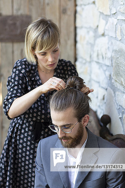 Frau frisiert jungen Mann in grauem Anzug