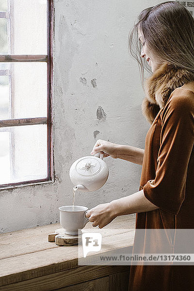 Lächelnde junge Frau gießt Tee in eine Tasse