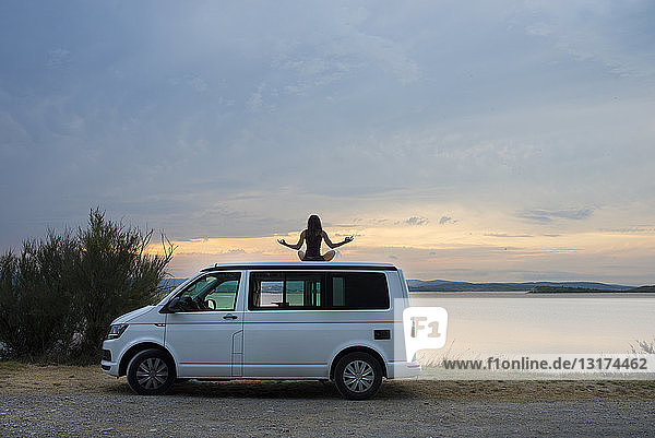 woman meditating on top of the van at sunset on the lake