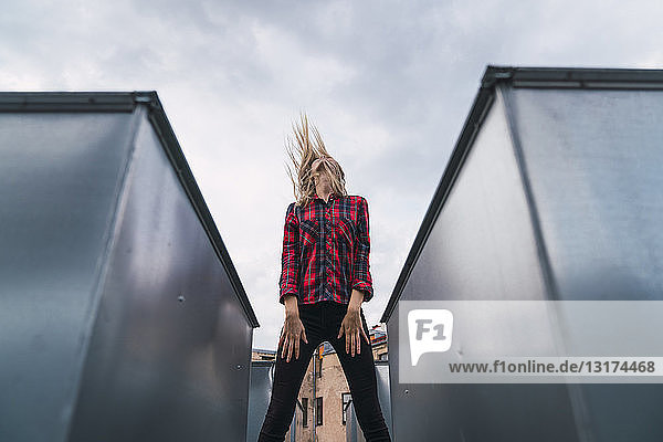 Modische junge Frau auf dem Dach wirft ihr Haar