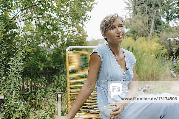 Frau sitzt im Garten mit einer Tasse Kaffee