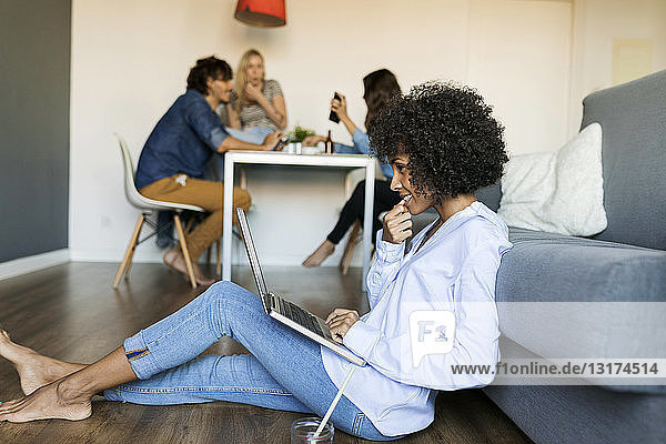 Woman sitting on floor using laptop with friends in background