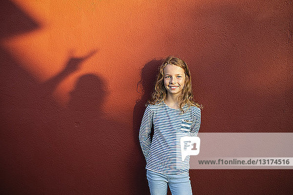 Portrait of smiling girl in front of a red wall with shadow