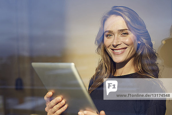Porträt einer lachenden Frau mit Tablette hinter einer Fensterscheibe