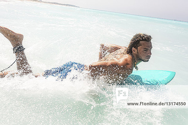 Young surfer paddling  lying on his surfboard