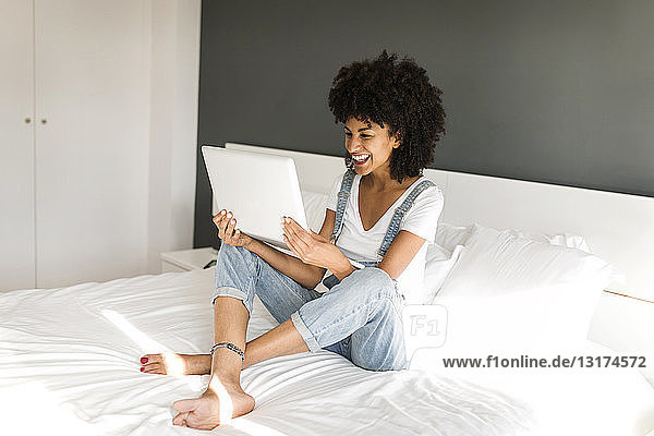 Happy woman sitting on bed looking at tablet
