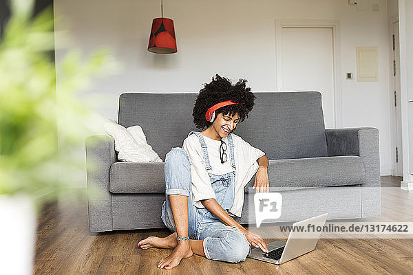 Lächelnde Frau sitzt zu Hause mit Kopfhörern und Laptop