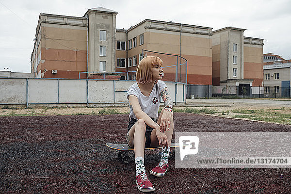 Coole junge Frau sitzt auf Carver-Skateboard im Freien