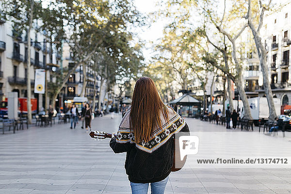 Red-haired woman playing the guitar in the city  rear view