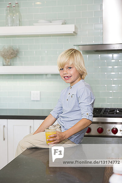 Glücklicher Junge in der Küche mit einem Glas Orangensaft