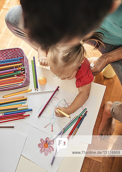 Kleines Mädchen zeichnet mit Farbstift  während ihr Vater sie beobachtet  Draufsicht