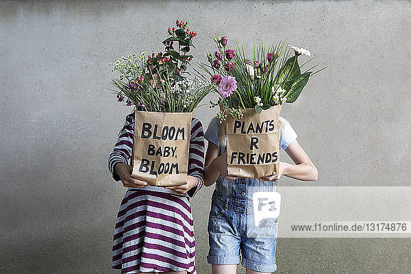 Zwei nebeneinander stehende Mädchen verstecken sich hinter Papiertüten mit Blumen