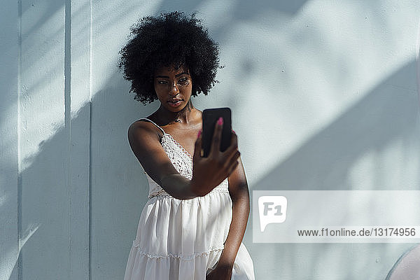 Young woman wearing white dress taking a selfie at a wall
