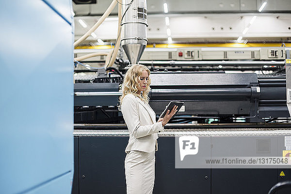 Frau benutzt Tablette an Maschine in Fabrikhalle