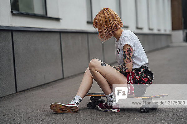 Junge Frau sitzt auf Carver-Skateboard auf dem Bürgersteig