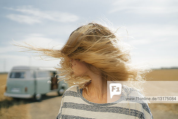Blonde junge Frau im Wohnmobil in ländlicher Landschaft schüttelt ihr Haar