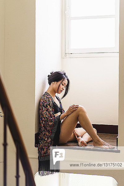 Attraktive junge Frau in Dessous  die in einer Nische am Fenster sitzt