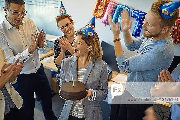 Kollegen mit einer Geburtstagsfeier im Büro mit Kuchen und Partyhüten