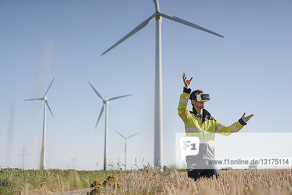 Ingenieur  der mit einer VR-Brille auf einem Feld in einem Windpark steht
