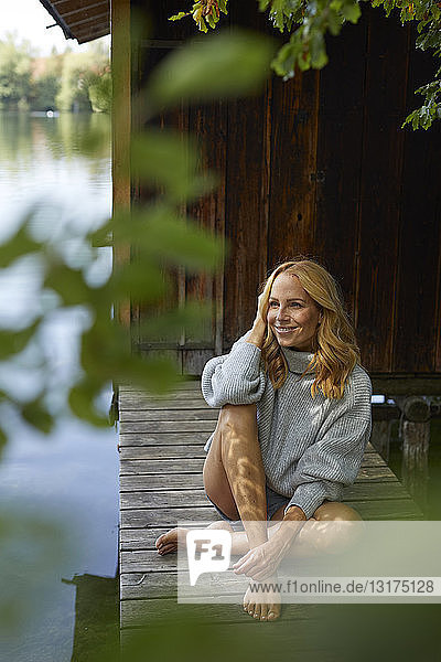 Entspannte Frau sitzt auf einem Holzsteg an einem abgelegenen See