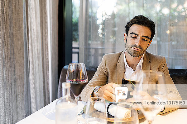 Mann sitzt am Tisch in einem Restaurant und benutzt sein Handy