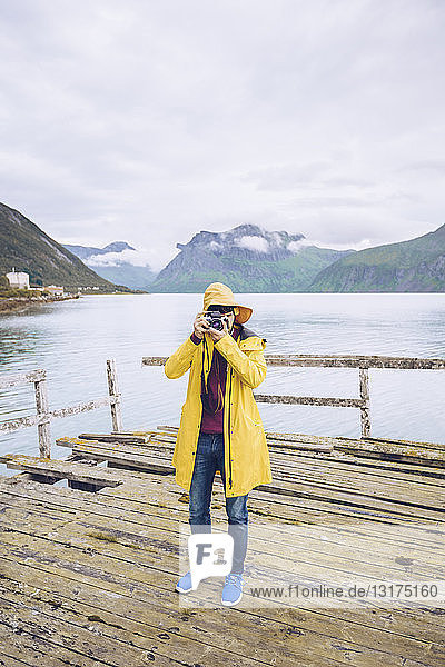 Norwegen  Senja  Mann steht auf einem baufälligen Steg an der Küste und macht ein Foto