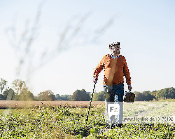 Senior man carrying traveling bag  walking in the fields