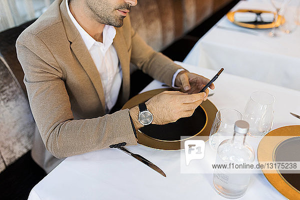 Nahaufnahme eines Mannes  der in einem Restaurant am Tisch sitzt und ein Mobiltelefon benutzt