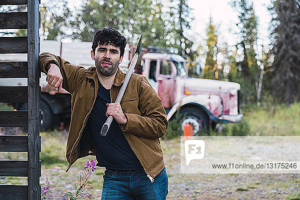Young man holding axe  standing in front of a broken truck
