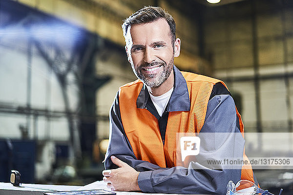 Porträt eines lächelnden Mannes in der Fabrik  der eine Sicherheitsweste trägt